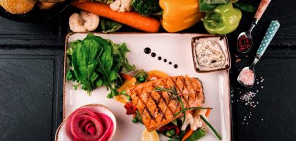 Top view of grilled salmon served with vegetables, herbs, and fresh bread. Perfect for a healthy meal.