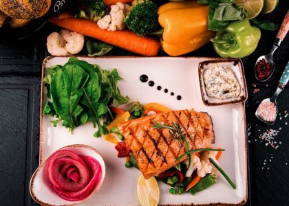 Top view of grilled salmon served with vegetables, herbs, and fresh bread. Perfect for a healthy meal.