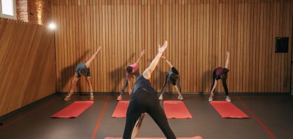 Yoga class with diverse adults stretching on mats in a cozy wooden studio.